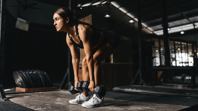 A woman performing a dumbbell deadlift in a gym, focusing on strength training
