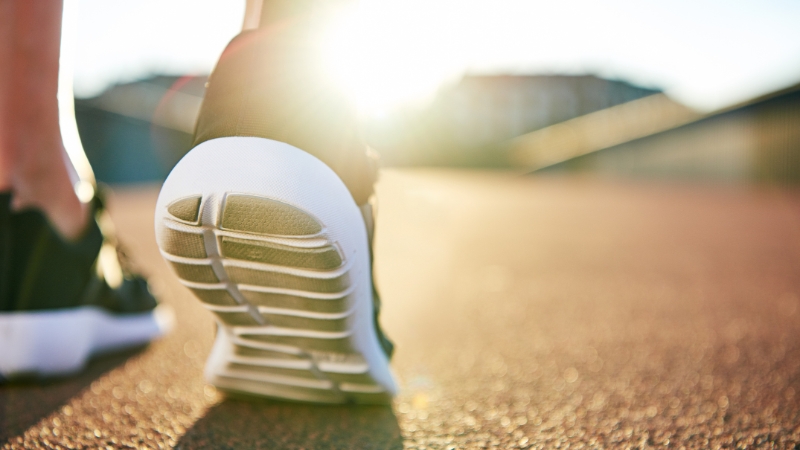 Close-up of a runnerโs shoe on pavement with sunlight in the background