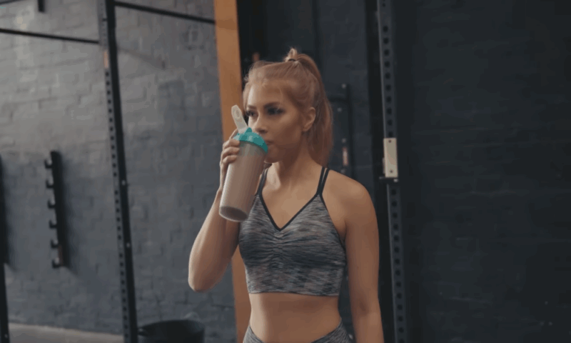Woman in workout clothes drinking a protein shake at the gym.