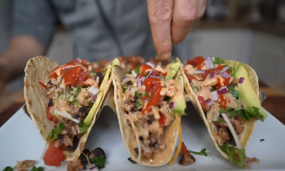 Close-up of three vegan tacos filled with rice, beans, avocado, onions, and sauce.