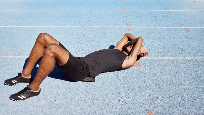 An exhausted athlete lies on a track with arms over the face after intense training