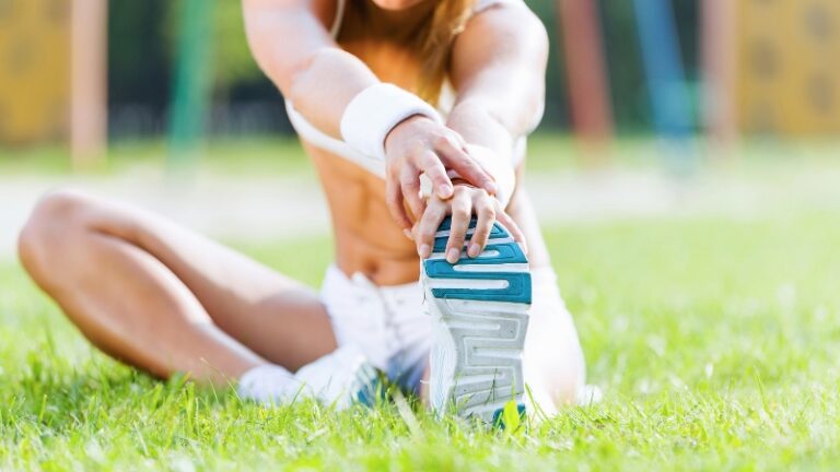 Female athlete sitting on grass reaching forward to stretch her leg and touch her shoe