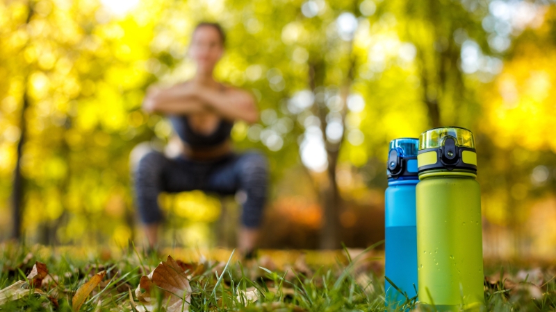 Two water bottles on grass with a person exercising outdoors in the background
