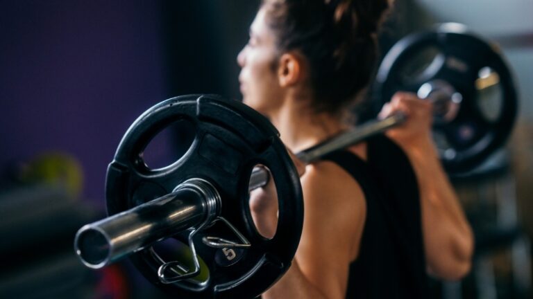 Close-up of a woman lifting a barbell with weight plates at the gym
