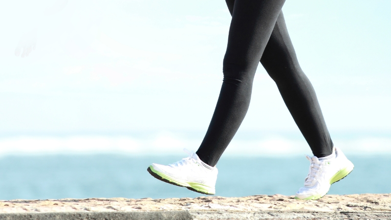 A person walks outdoors near the water, wearing athletic shoes and black leggings