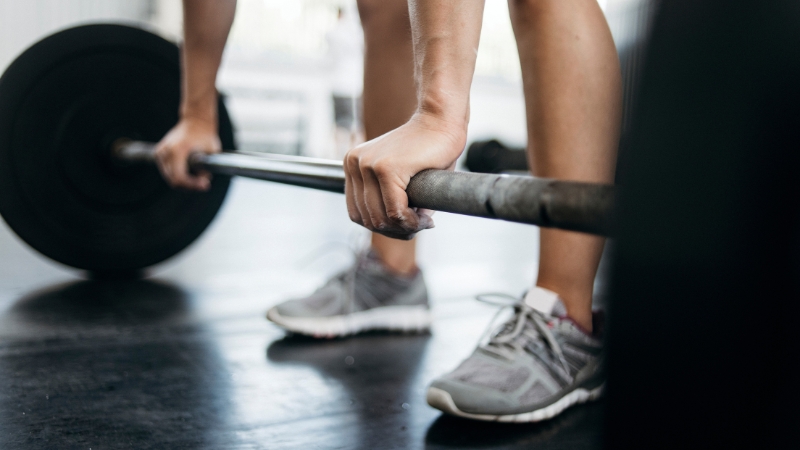 A person gripping a barbell on the gym floor while preparing to lift during a resistance training workout