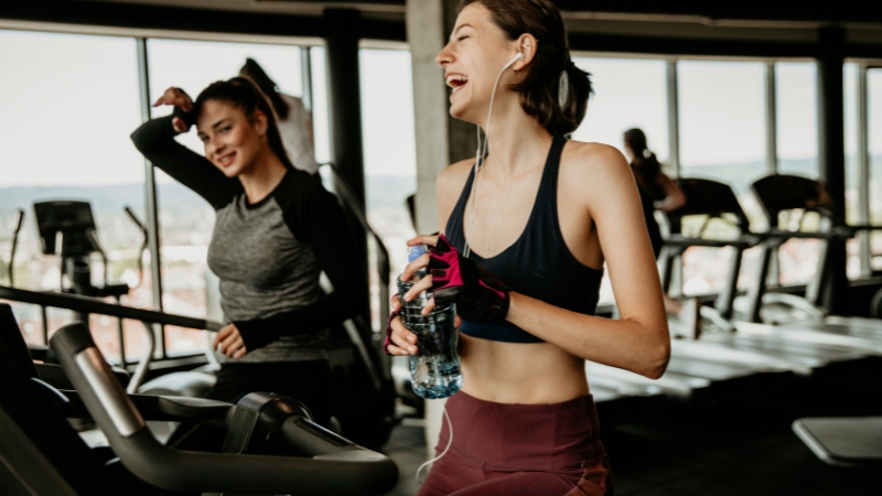 Two women laughing and relaxing during a cardio session at the gym