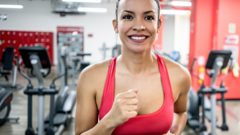 A woman jogging indoors with a confident smile as she notices her first results in a gym