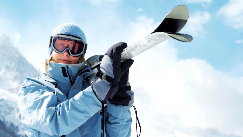 A skier holds her skis in cold mountain air during a high-altitude day