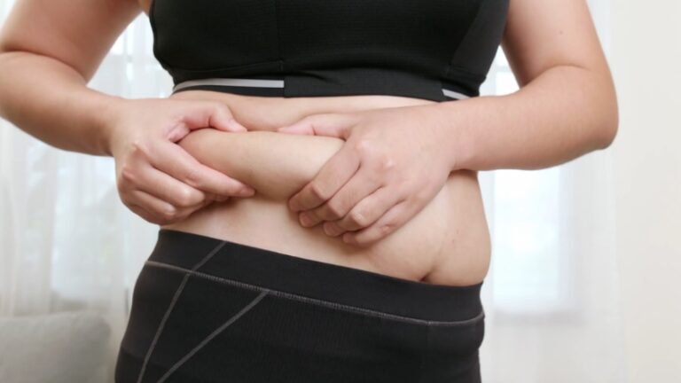 Person in workout clothes pinches belly fat at the waist