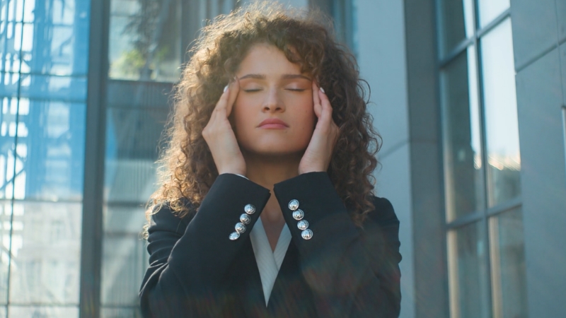 A woman holds her temples outside an office building during a moment of stress