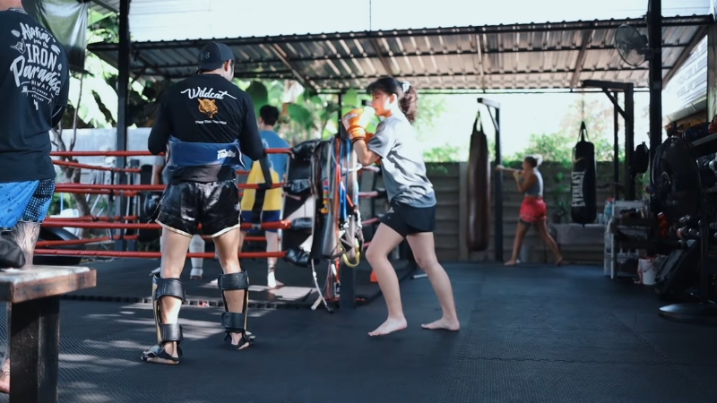 A woman practices Muay Thai drills with a coach in an open gym