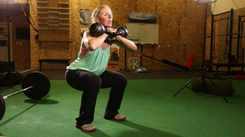 A woman performs a weighted squat indoors to build strength that supports skiing