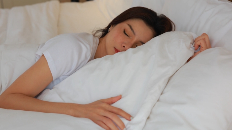 A woman sleeps on a white bed with her arm resting on a pillow