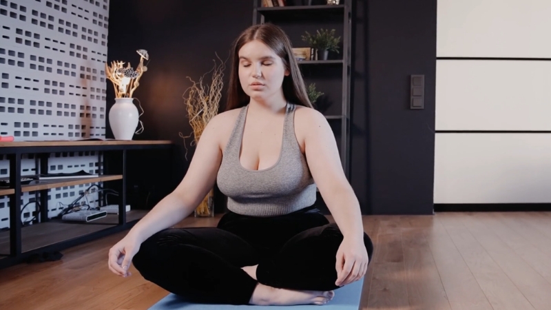 Woman sits cross legged on a yoga mat and focuses on calm breathing at home