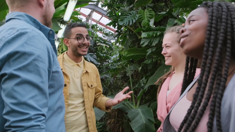 A group of friends talk and smile together in a lush indoor garden