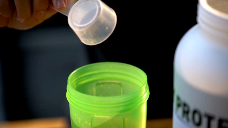Scoop of protein powder being added to a shaker for whey vs plant-based protein absorption comparison