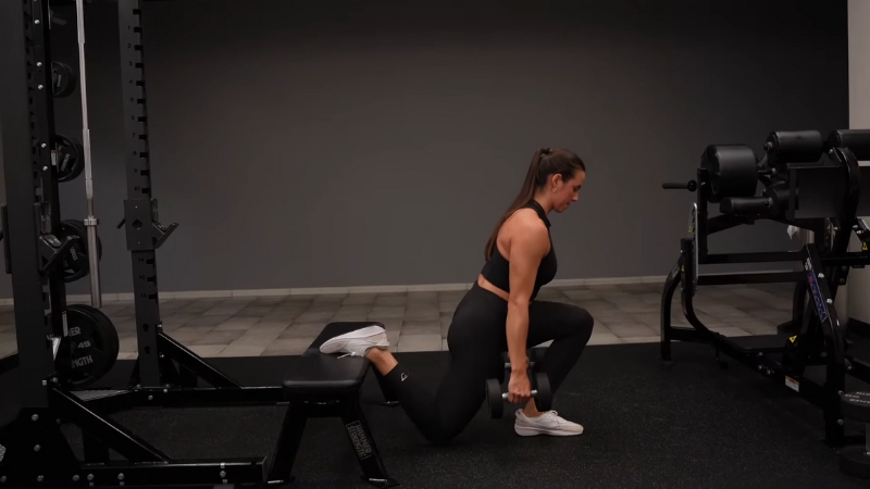 Woman perform Bulgarian split squat with dumbbells, rear foot elevated on bench