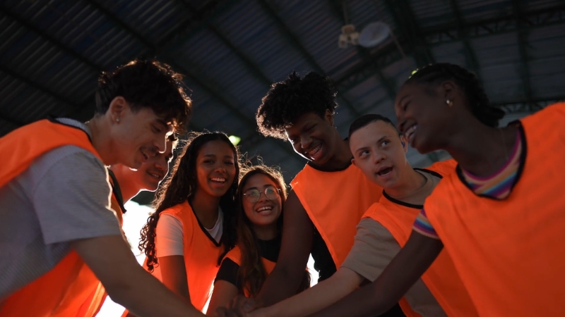 Youth athletes in orange vests huddle together before a school-based sports practice