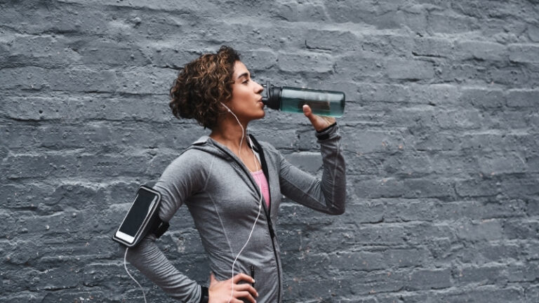 A woman drinks a hydration drink that supports electrolytes and energy after exercise