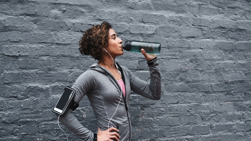 A woman drinks a hydration drink that supports electrolytes and energy after exercise