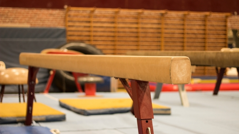 Balance beam set inside a gymnastics training hall with mats and equipment around it