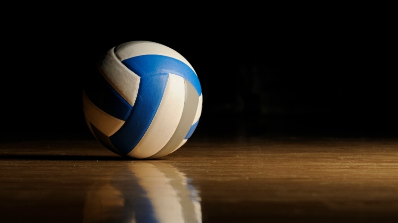 Volleyball rests on an indoor court floor under focused lighting before a training session