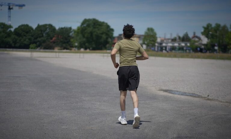 A person runs on a wide, open road under a clear blue sky