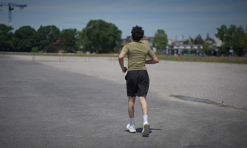 A person runs on a wide, open road under a clear blue sky