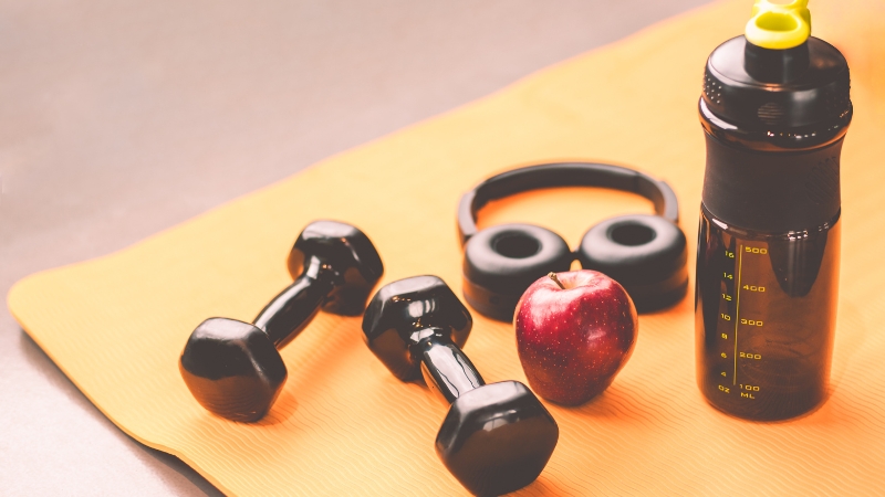 Dumbbells, water bottle, and apple show balance between fasting and strength training