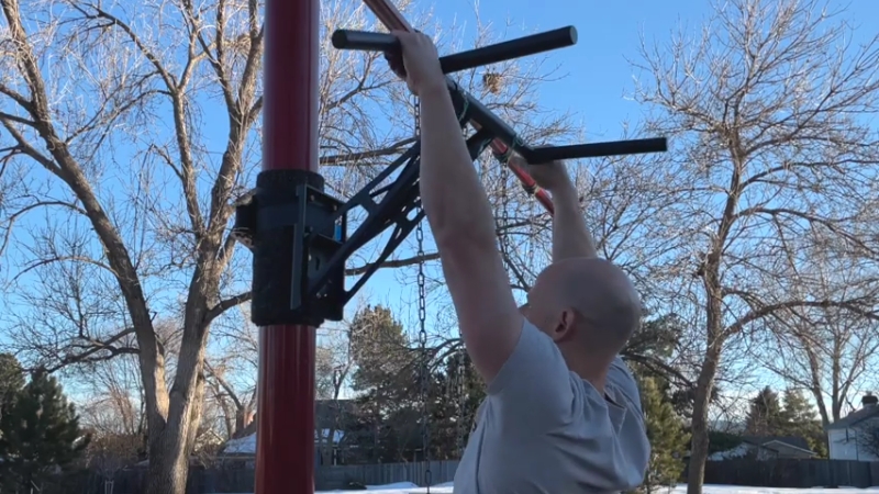 Man perform pull-ups on an outdoor pull-up and dip station mounted to a vertical post