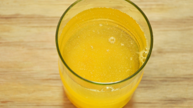 A glass of yellow electrolyte drink sits on a wooden surface