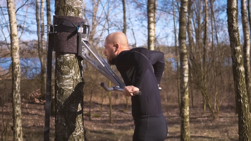 Man perform dips on a traditional pull-up and dip station mounted outdoors among trees