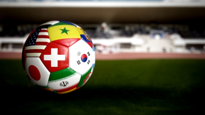Soccer ball with national flags sits on a field, symbolizing cultural differences between US and European sports