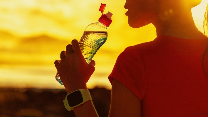 A person drinks an electrolyte beverage outdoors during warm weather