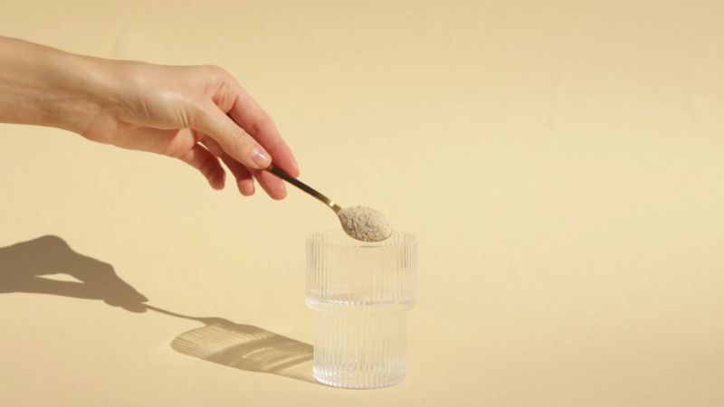 Spoon with collagen powder held over a glass on a neutral background