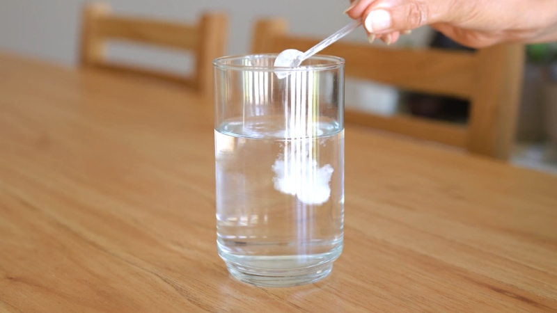 Collagen powder being mixed into a glass of water on a wooden table