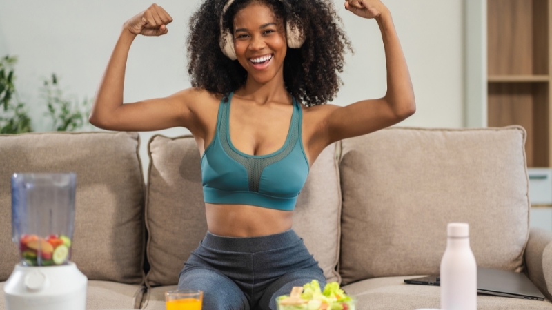 Woman flexing muscles at home with healthy meal and smoothie nearby