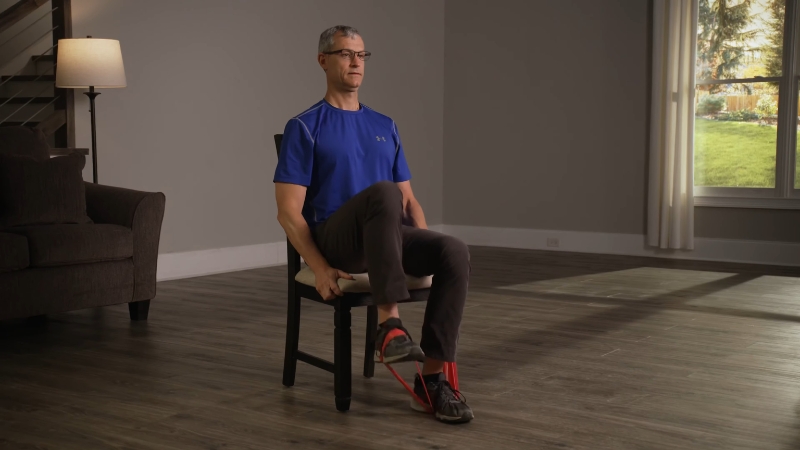 Man performs a seated rehab exercise with a resistance band at home