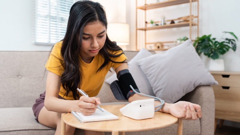 Woman checking blood pressure at home and writing down the result