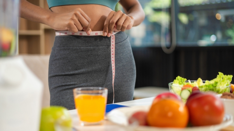 Woman measuring waist with tape near healthy food during a new weight-loss plan routine change