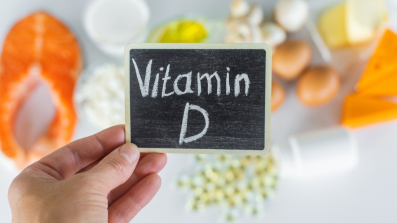 Hand holding a sign that says vitamin D with foods that support bone health in the background