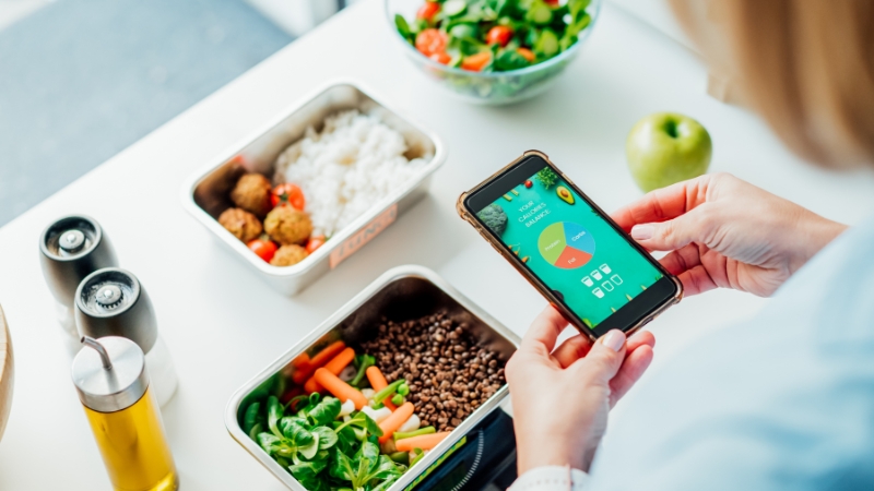 Person tracking meal macros on a smartphone while preparing balanced food containers