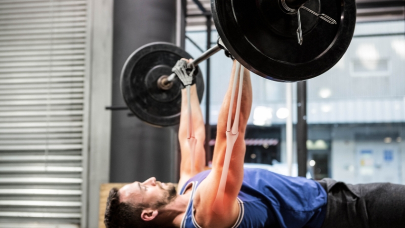 Man performing a barbell bench press in a gym, showing bone resilience under heavy weight training load