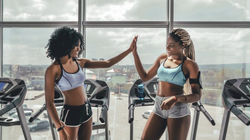 Two women high-five on treadmills in a gym