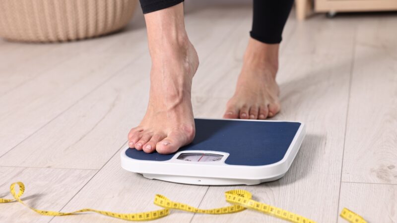 Woman steps onto a bathroom scale with a measuring tape on the floor