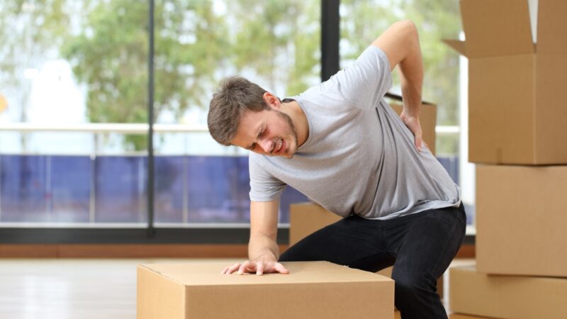 Man feels back pain while lifting a heavy box at home