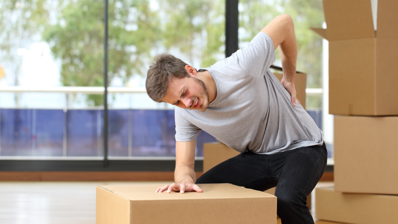 Man feels back pain while lifting a heavy box at home