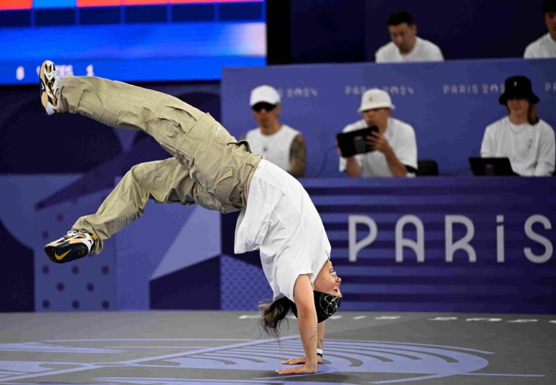 Breakdancer performing a one handed handstand move during a competition at the Paris Olympics