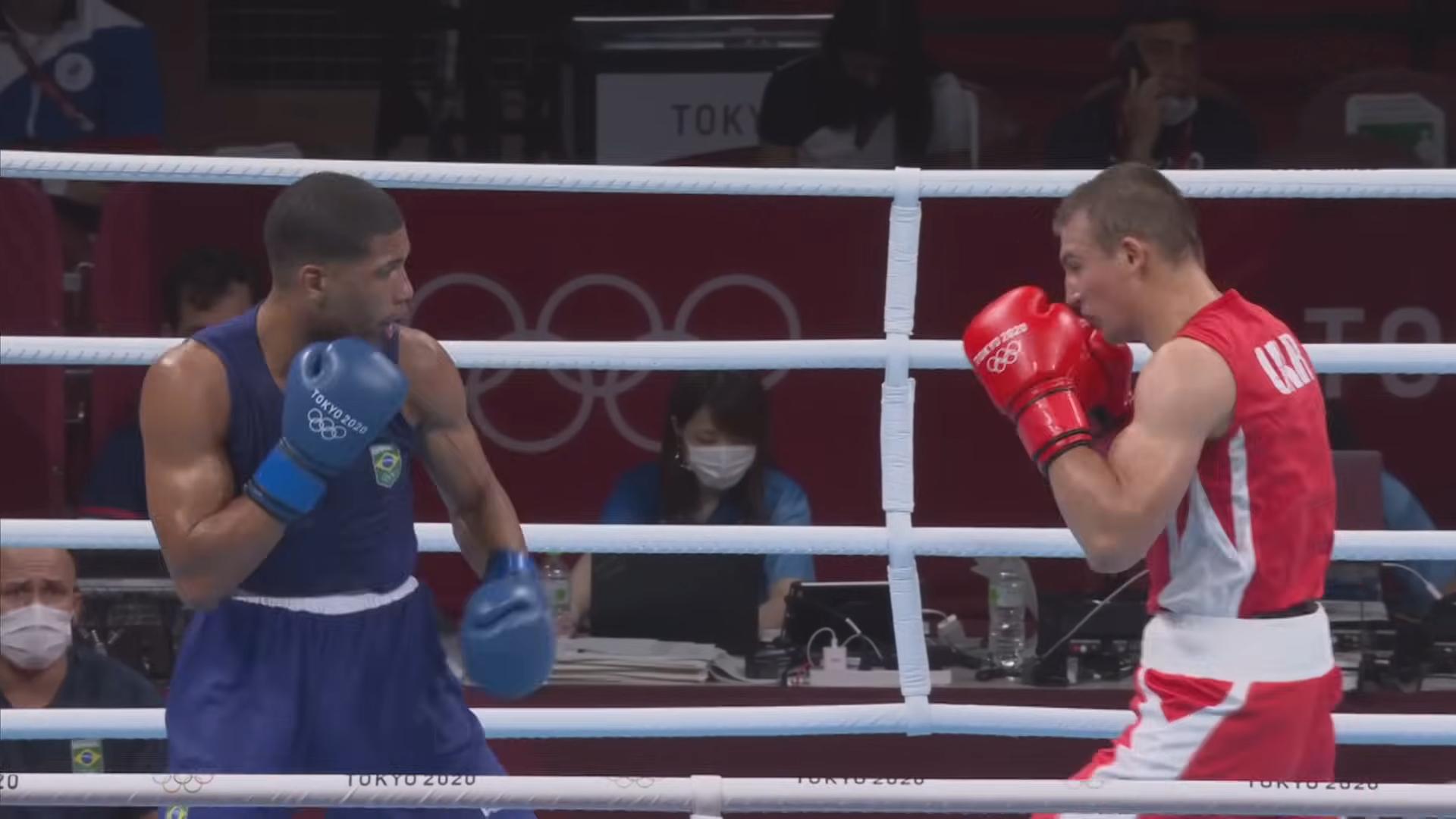 Two boxers in blue and red gear facing each other during an Olympic boxing match